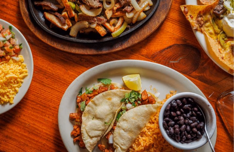 Overhead view of various Mexican dishes including fajitas, tacos, and nachos.