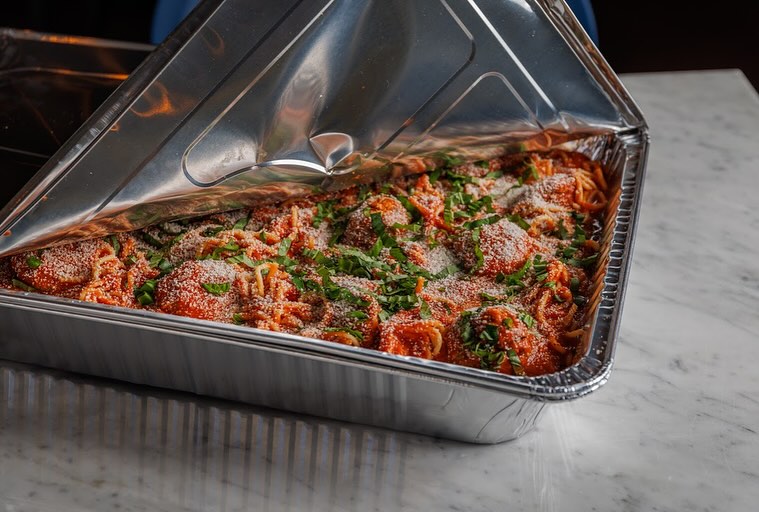 Spaghetti and meatballs in a foil tray with a partially lifted lid.