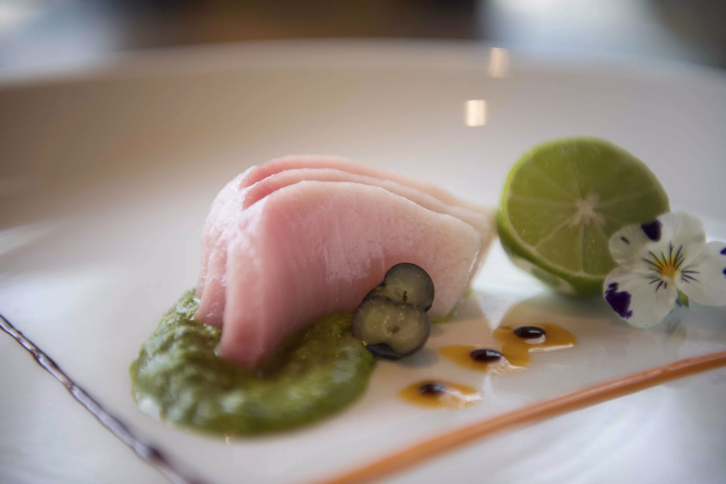 Raw fish, green sauce, lime, berries, and a white flower on a plate.