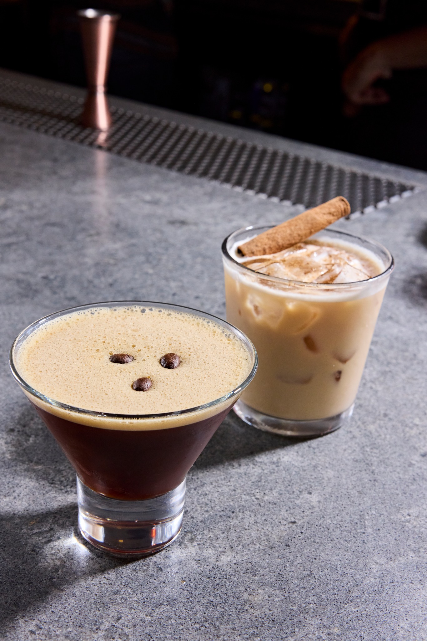 Dark foamy drink with coffee beans and iced drink with cinnamon stick.