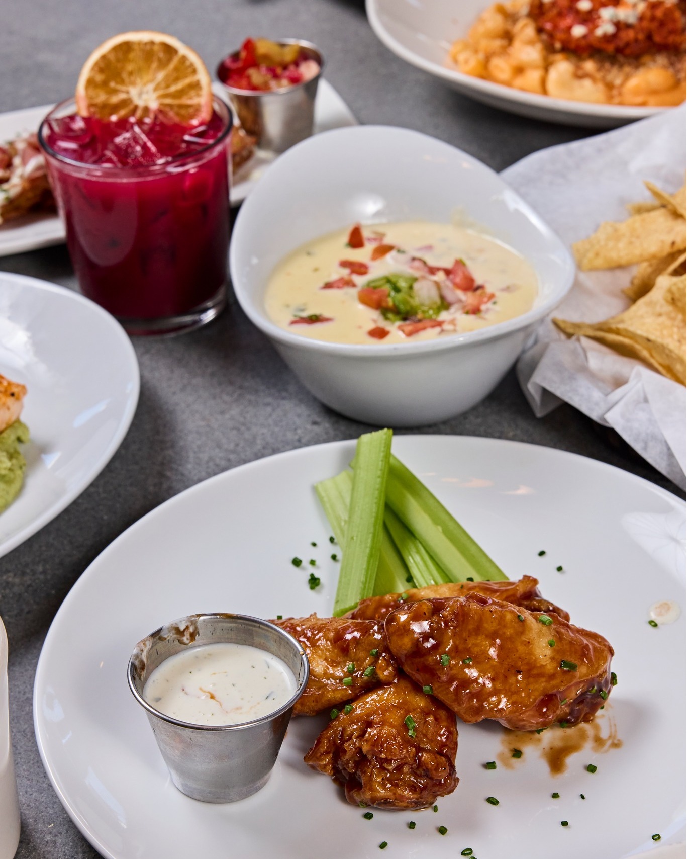 Chicken wings, celery, queso, tortilla chips, and a red drink.