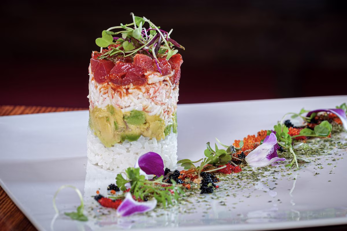 Layered rice, avocado, crab, and tuna stack, garnished with microgreens.