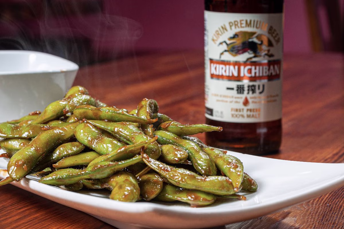 Steaming, sauced edamame on a plate, with Kirin Ichiban beer.