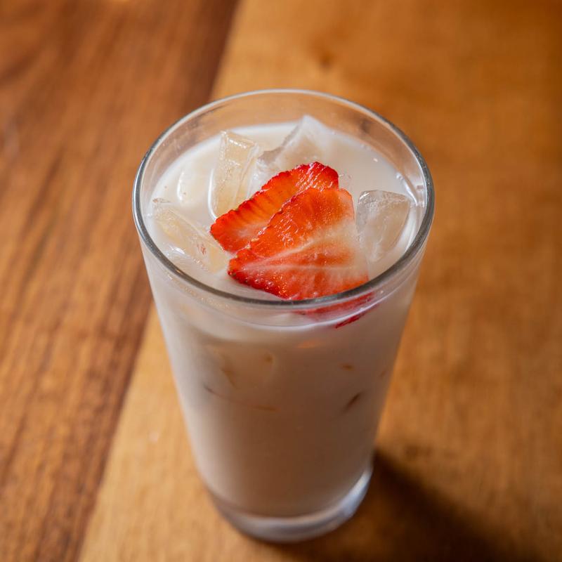 Iced milky drink in a glass with strawberry slices on a wooden surface.