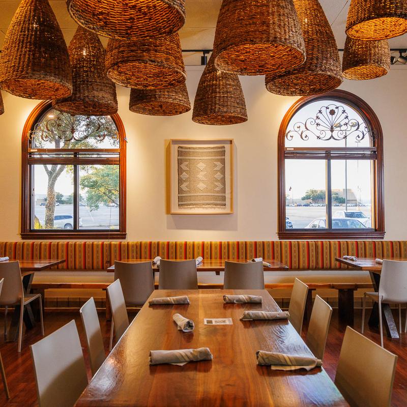 Restaurant dining area with woven basket lights, wooden tables, and windows.