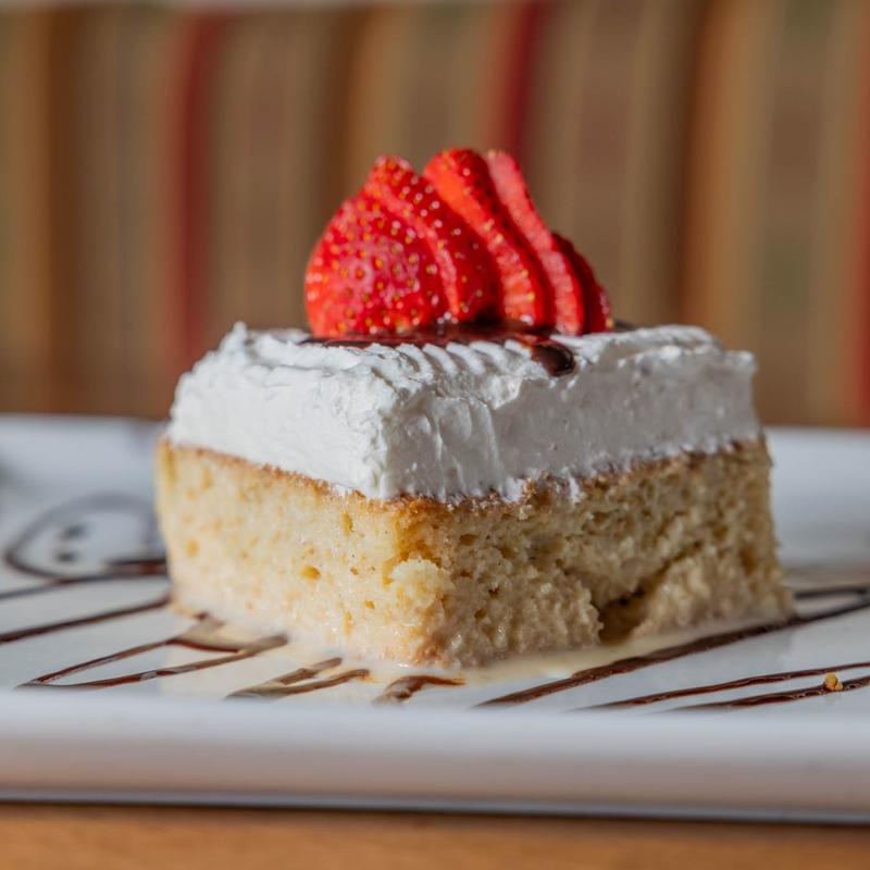 Cake slice with whipped cream, sliced strawberries, and chocolate drizzle.