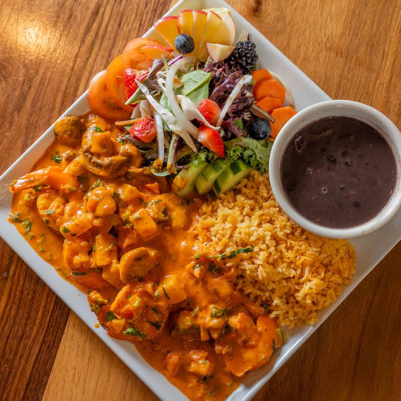 Plate of shrimp in sauce, yellow rice, black beans, and mixed salad.