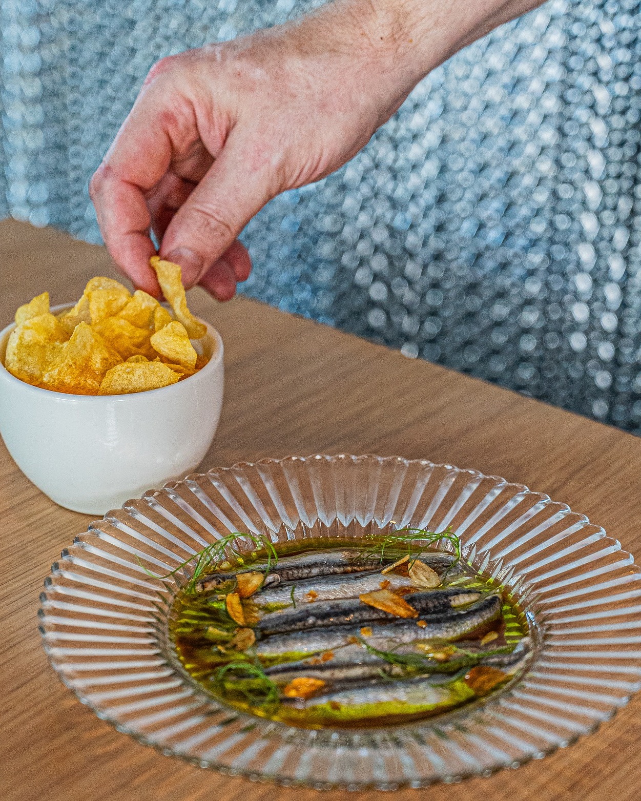 Hand picking a chip, beside a plate of marinated small fish.