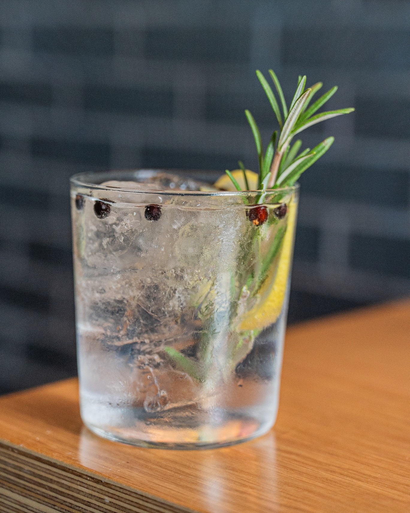Clear iced drink with rosemary, lemon slice, and dark berries.