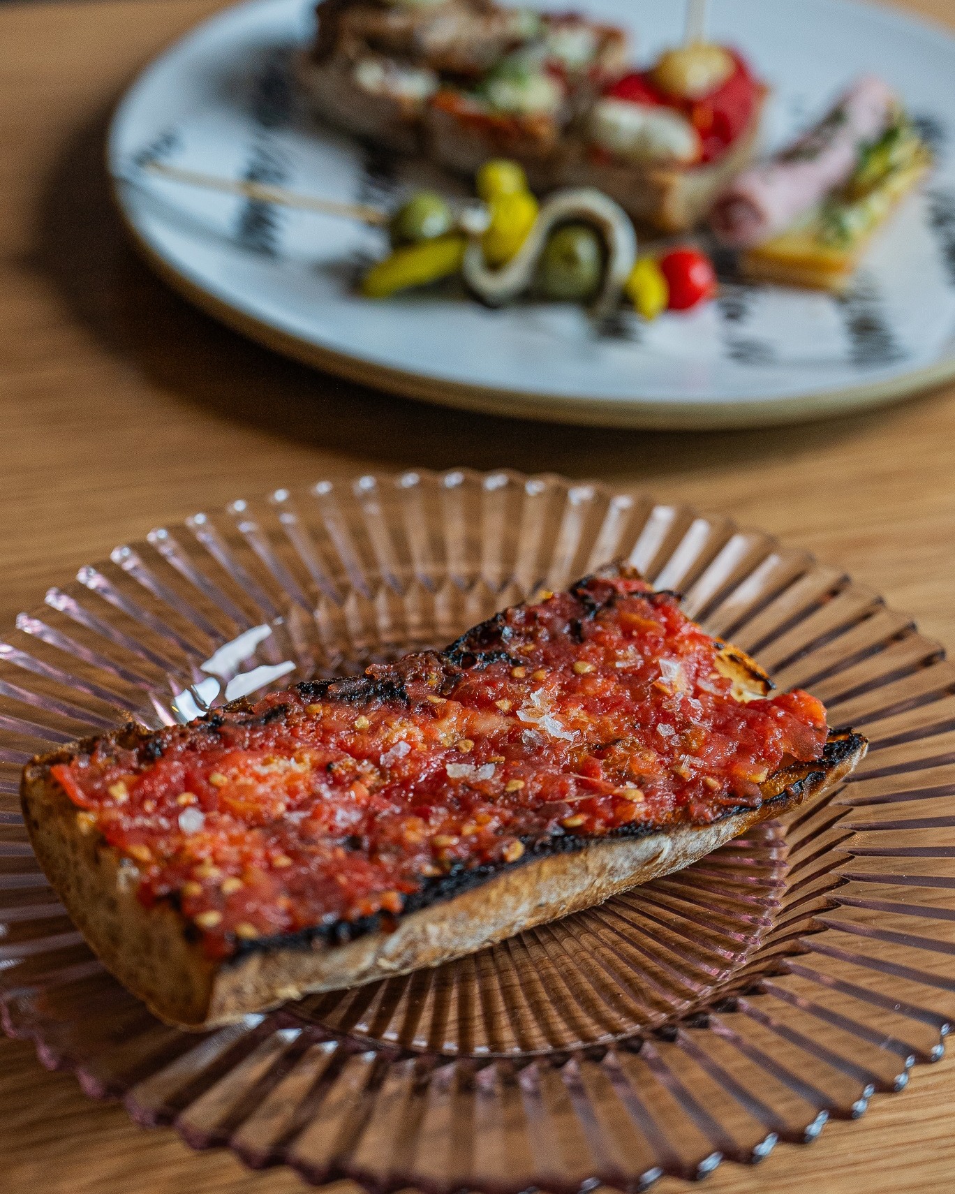 Toasted bread with tomato and salt, with tapas in the background.