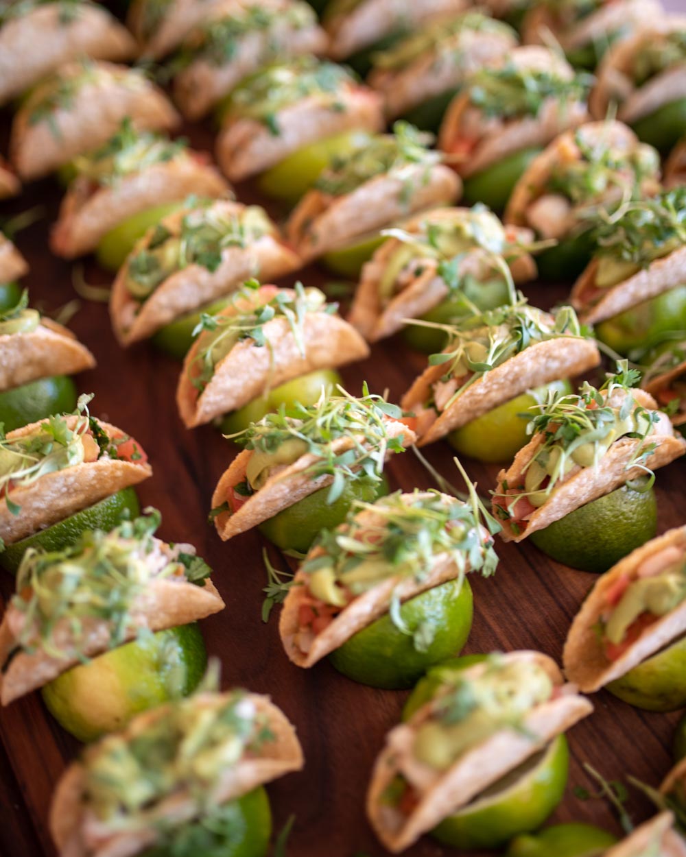 Mini tacos with avocado and sprouts, each resting on a lime half.