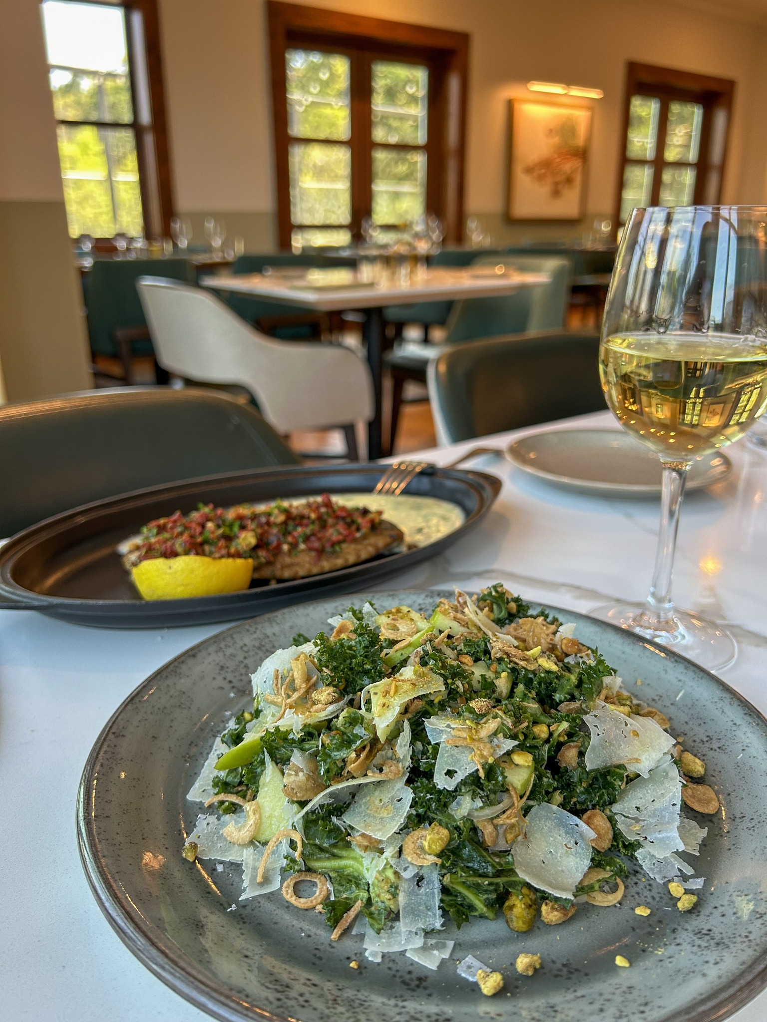 Kale salad, main dish, and white wine on a restaurant table.