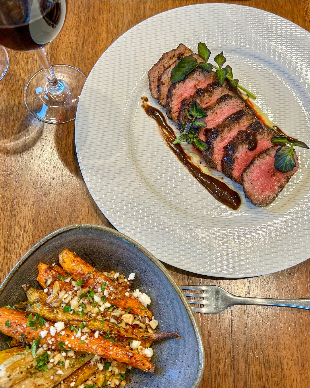 Sliced steak, roasted carrots, and red wine on a table.