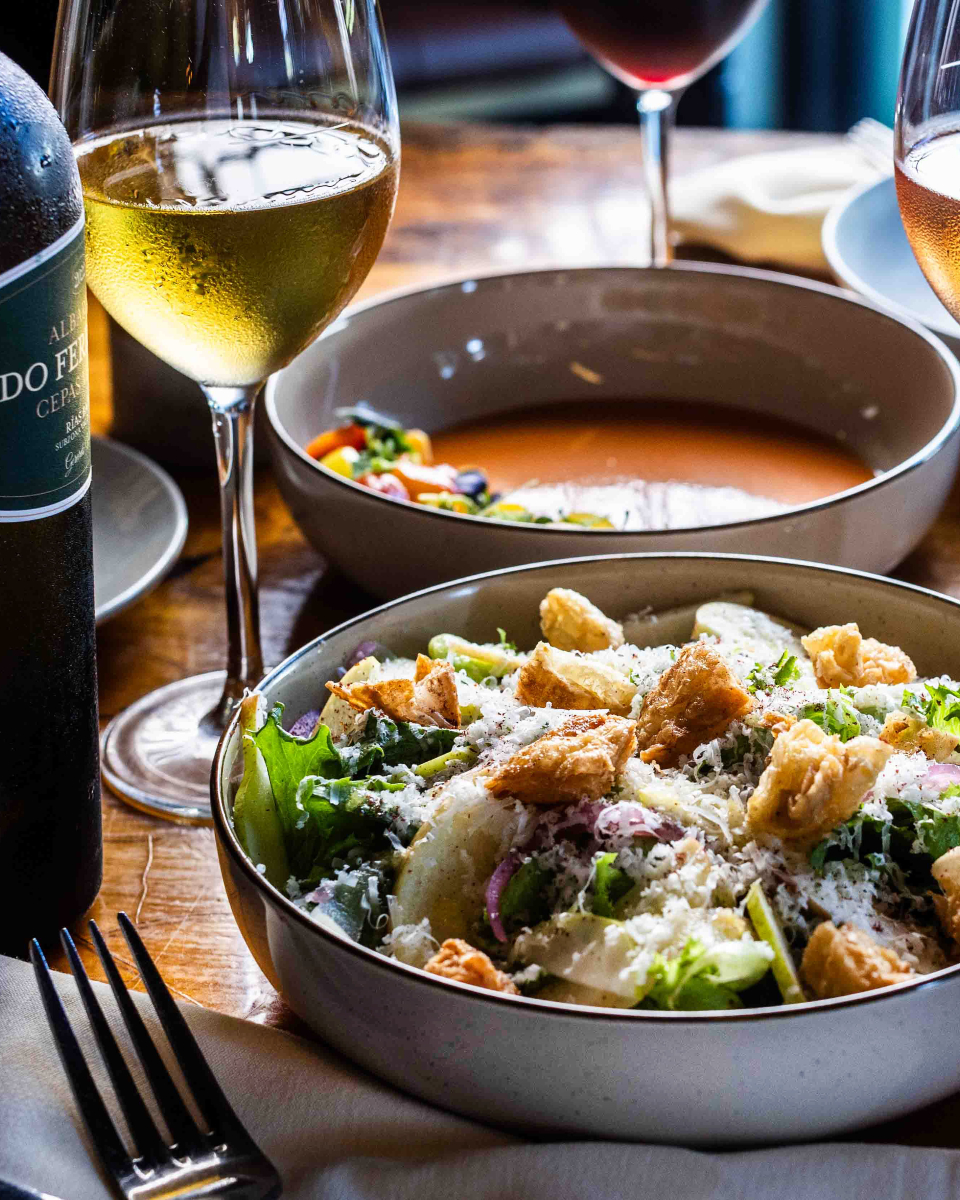White wine, salad, and soup bowls on a wooden table.