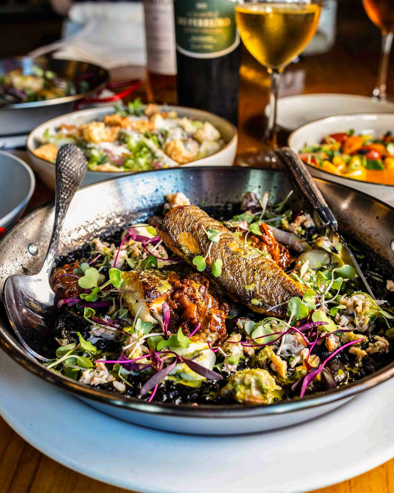 Pan of seared fish on dark grains with microgreens.