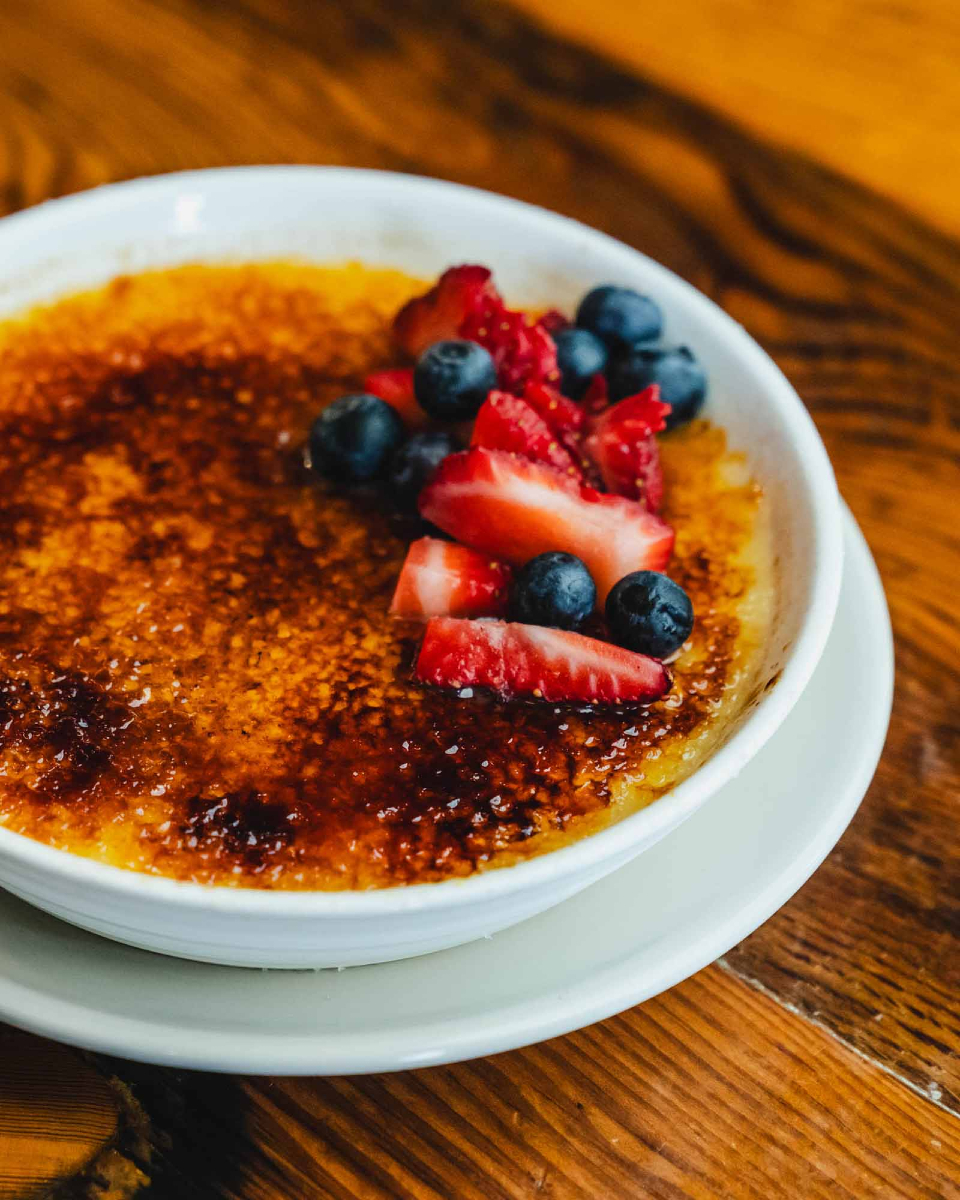 Crème brûlée with caramelized sugar, sliced strawberries, and blueberries.