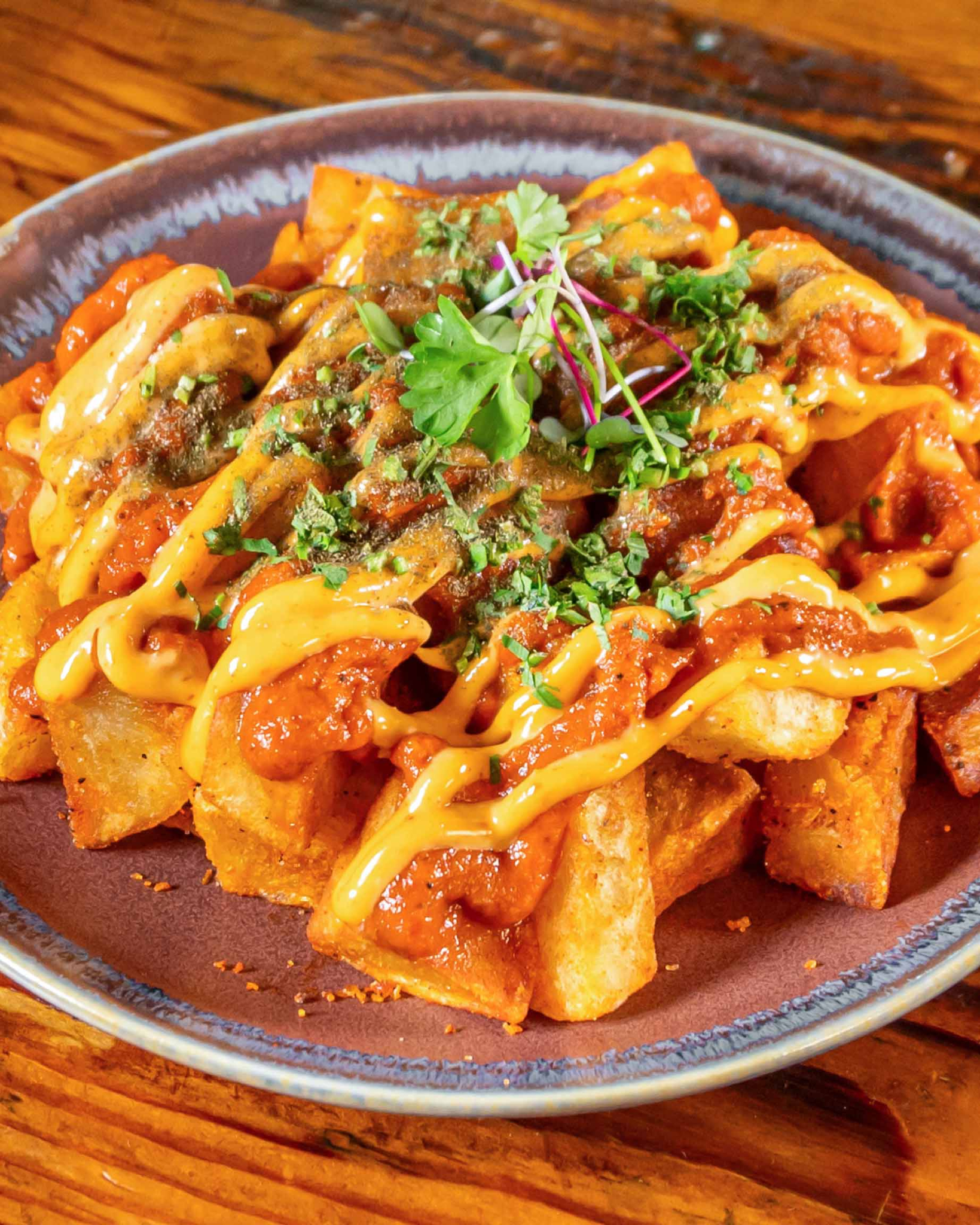A plate of patatas bravas with red and yellow sauces and fresh herbs.