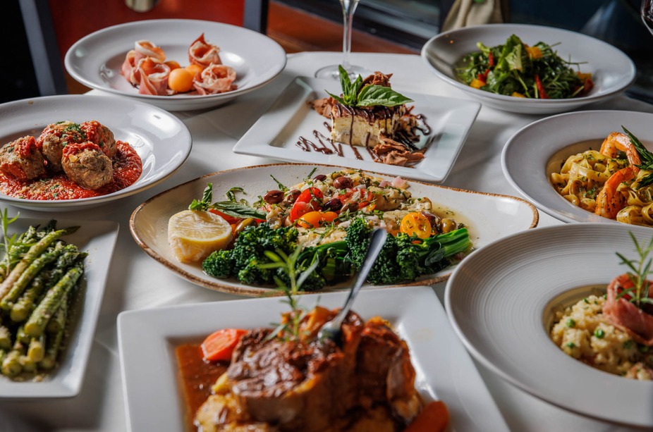 Numerous plates of diverse Italian restaurant dishes on a white tablecloth.