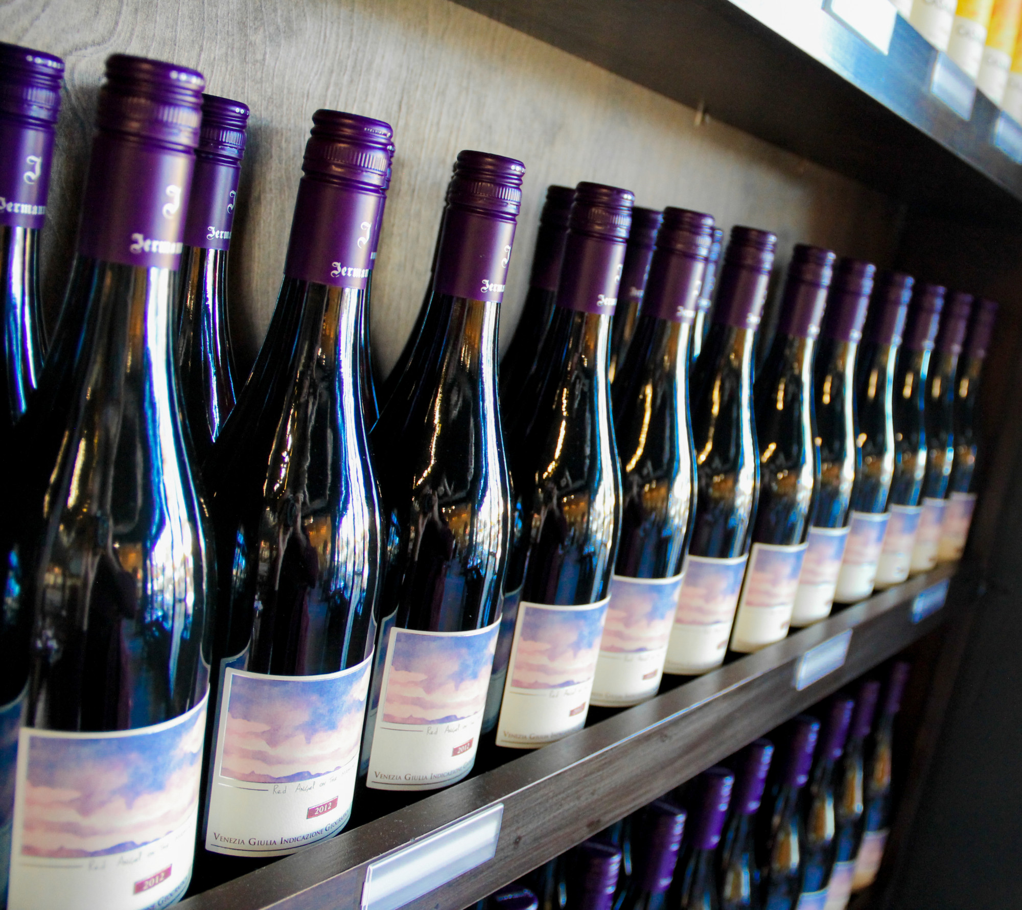 Rows of Jermann wine bottles with purple caps on wooden shelves.
