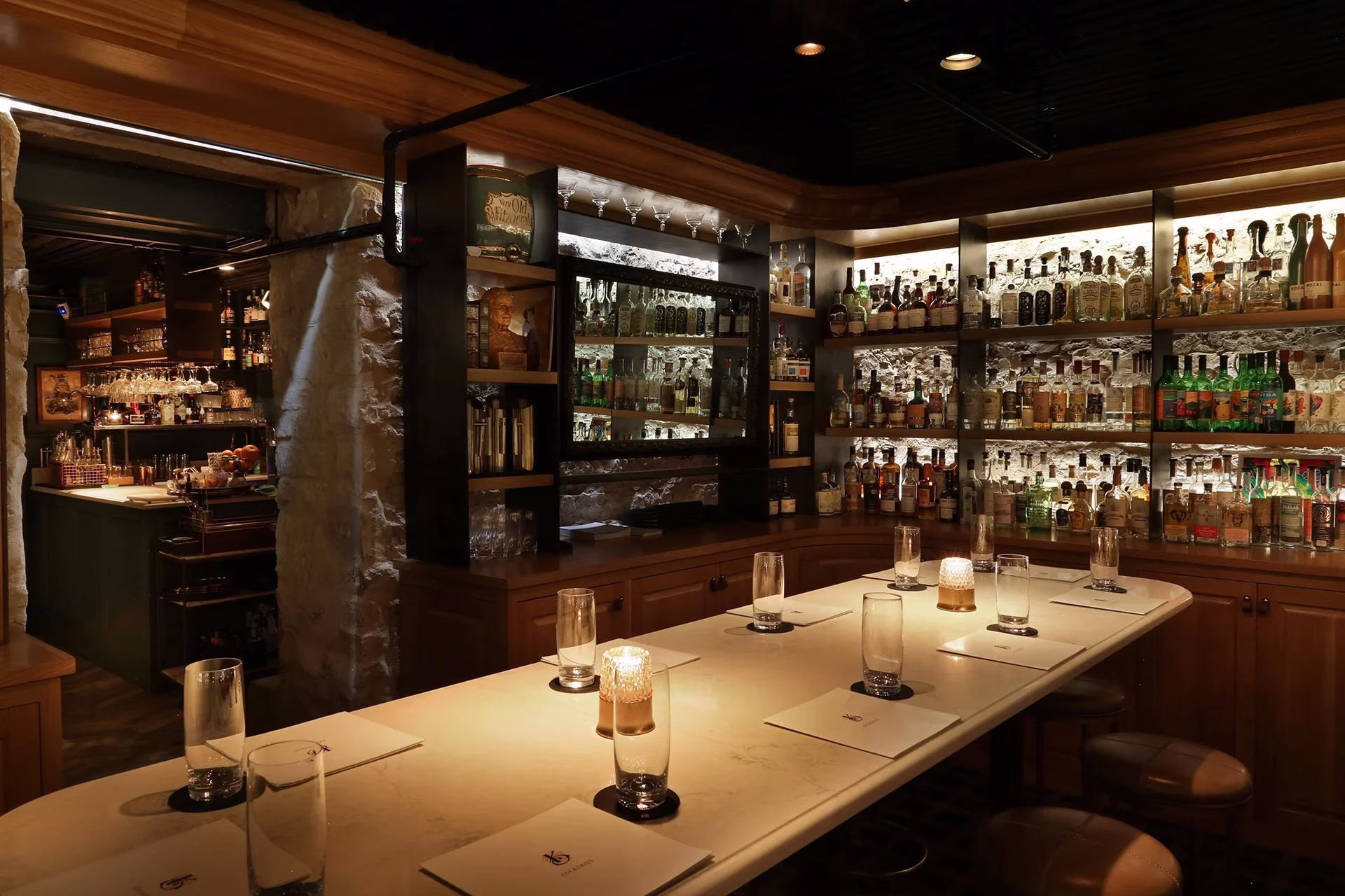 Dimly lit bar interior with a long counter and many liquor bottles.