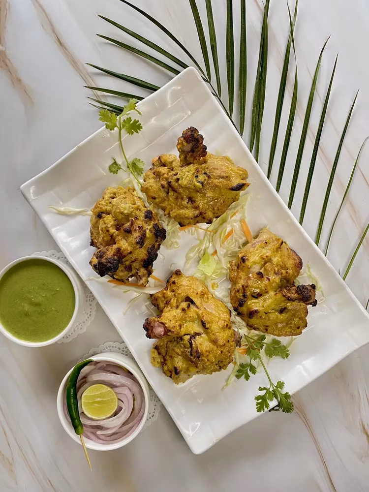 Four yellow chicken pieces with green sauce, onions, and lime.