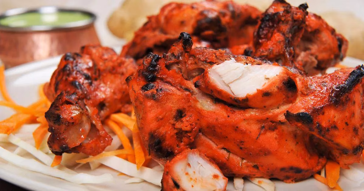 Vibrant red chicken pieces, charred, on shredded vegetables with green sauce.