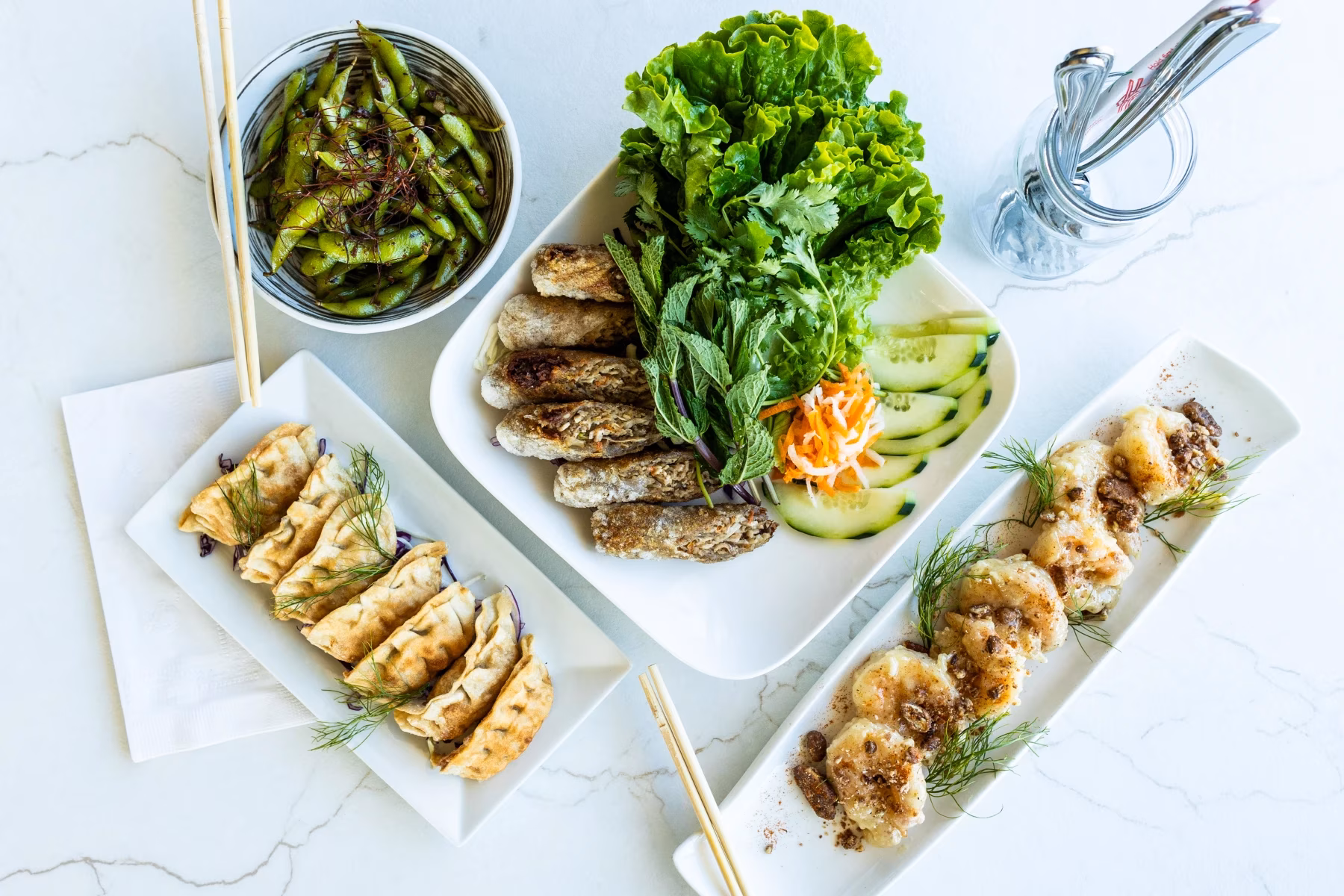 Assortment of edamame, spring rolls, dumplings, and shrimp on marble.