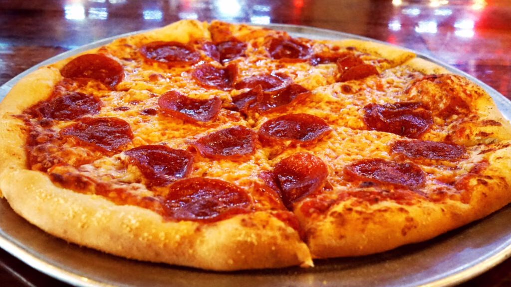 A whole pepperoni pizza with melted cheese on a metal tray.
