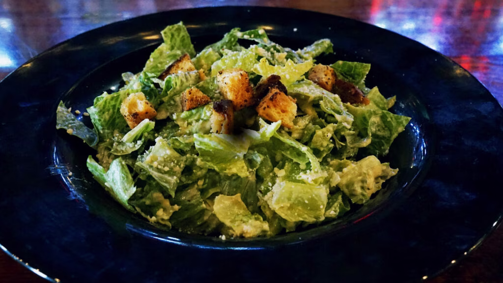 A Caesar salad with croutons and cheese in a dark blue bowl.