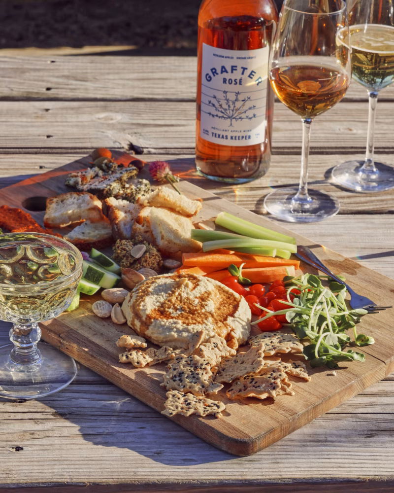 Rosé wine bottle, glasses, and assorted snacks on a wooden table.