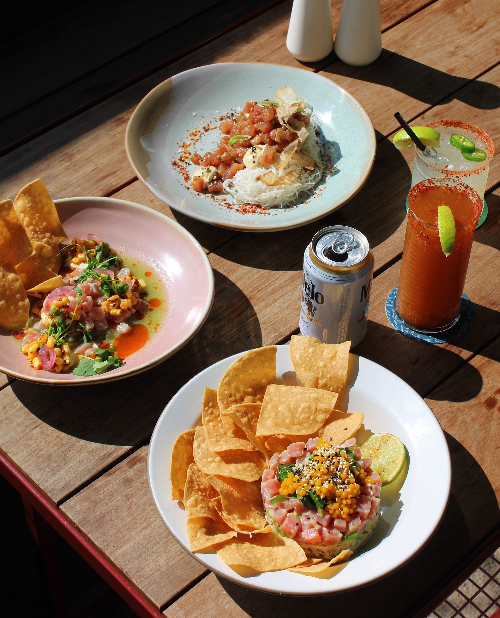 Three plates of seafood dishes, tortilla chips, beer, and cocktails.