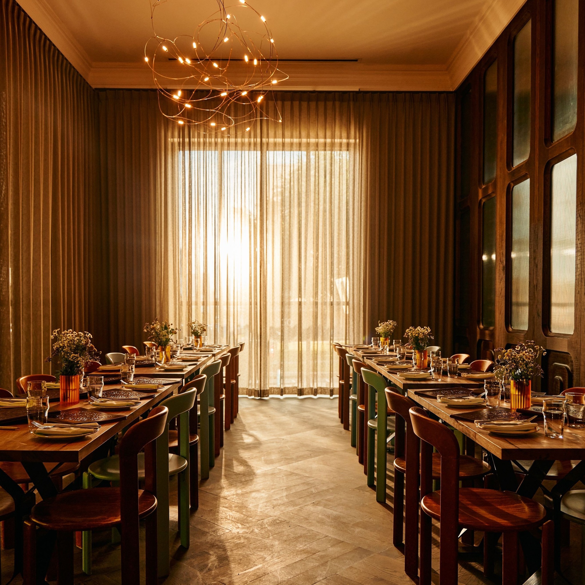 Dining room with set tables, a modern chandelier, and bright window.