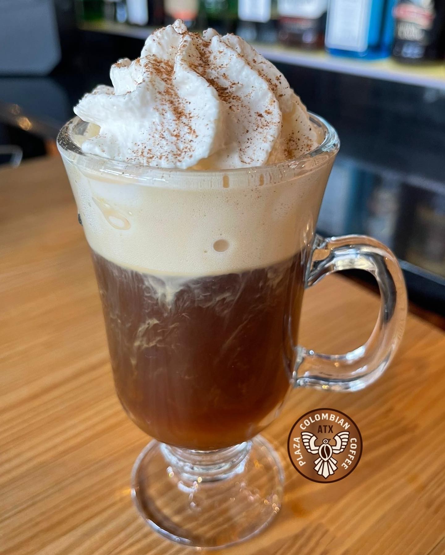 Dark coffee drink topped with foam and whipped cream in glass mug.
