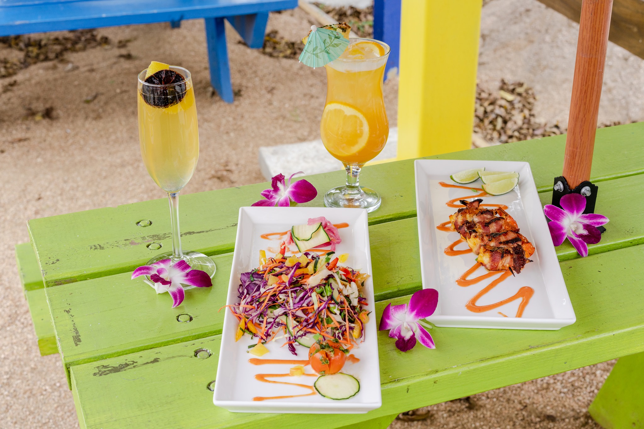 Tropical drinks and dishes with orchids on a green picnic table.