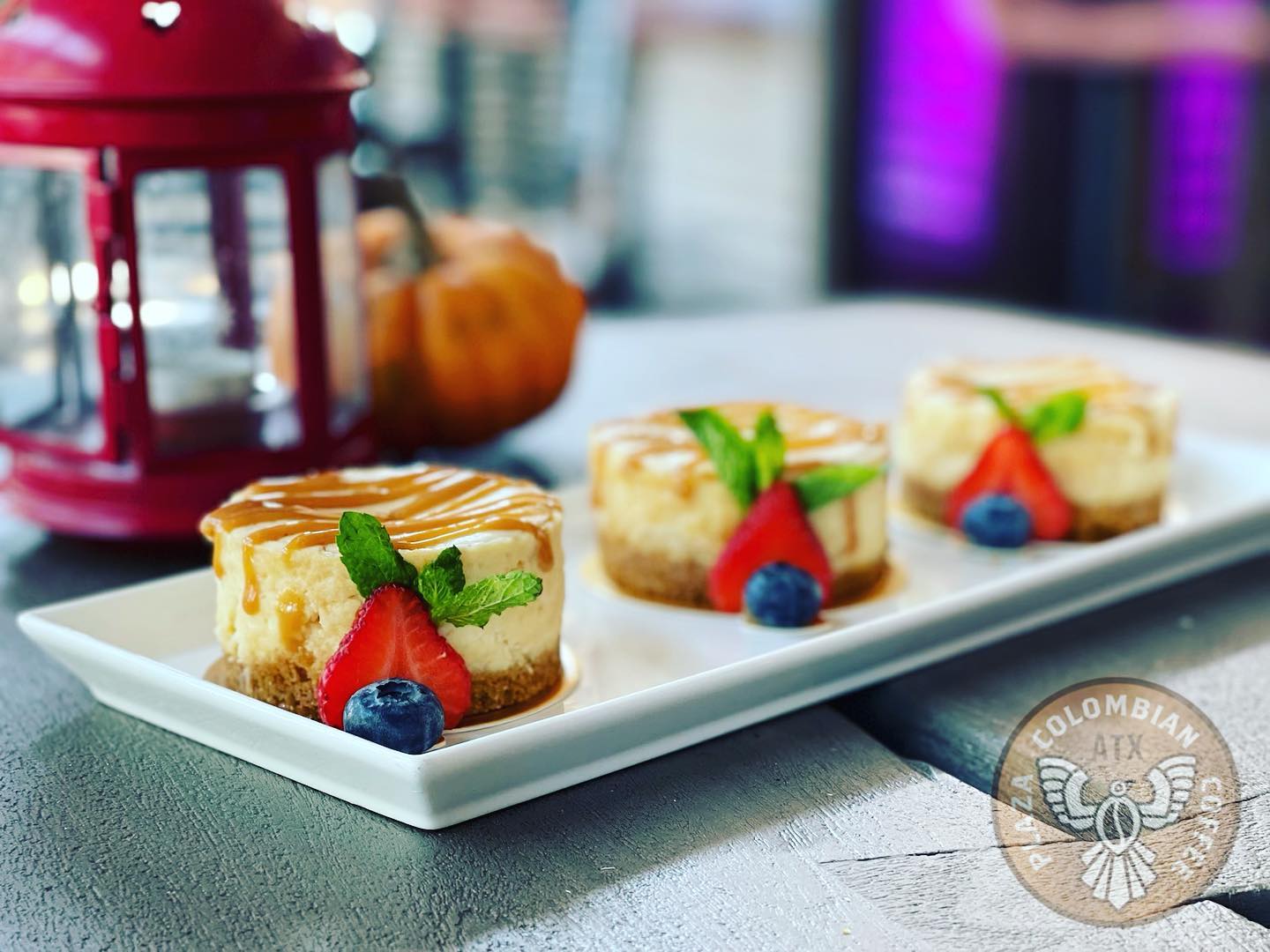 Three individual cheesecakes topped with caramel, berries, and mint.
