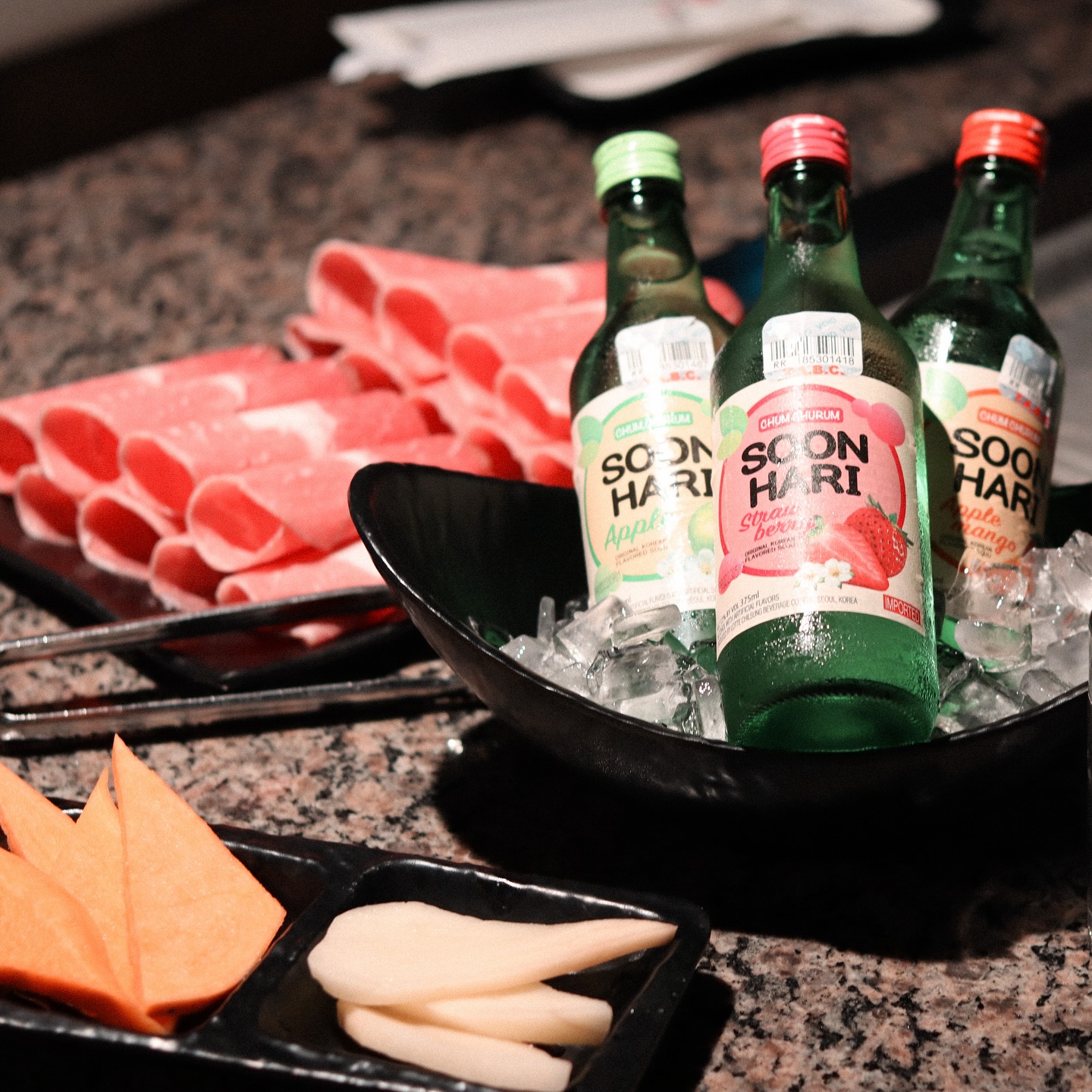 Three Soon Hari soju bottles on ice with raw meat and vegetables.