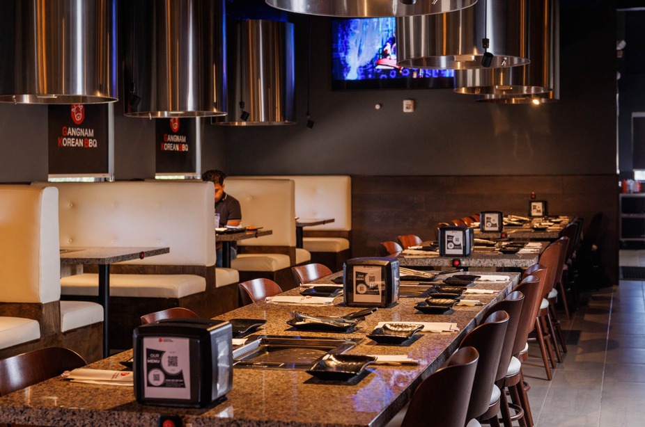 Restaurant interior with long tables, grills, and exhaust hoods.
