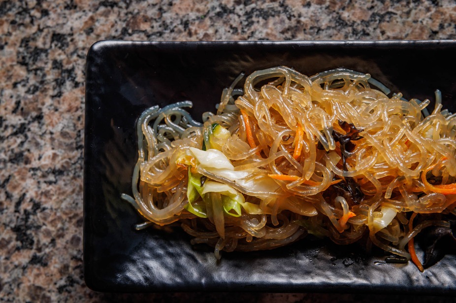 Translucent noodles, cabbage, and carrots in a black rectangular dish.