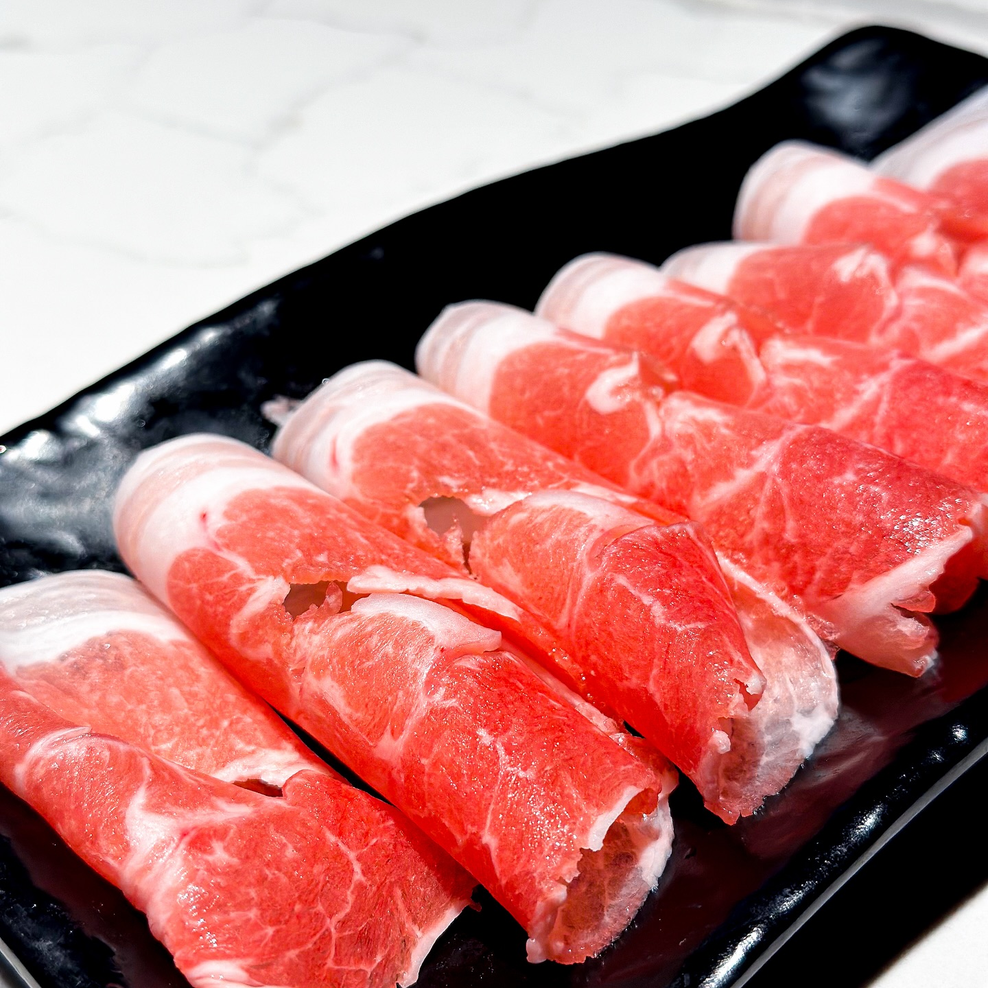 Raw, thinly sliced meat rolls with marbling on a black plate.
