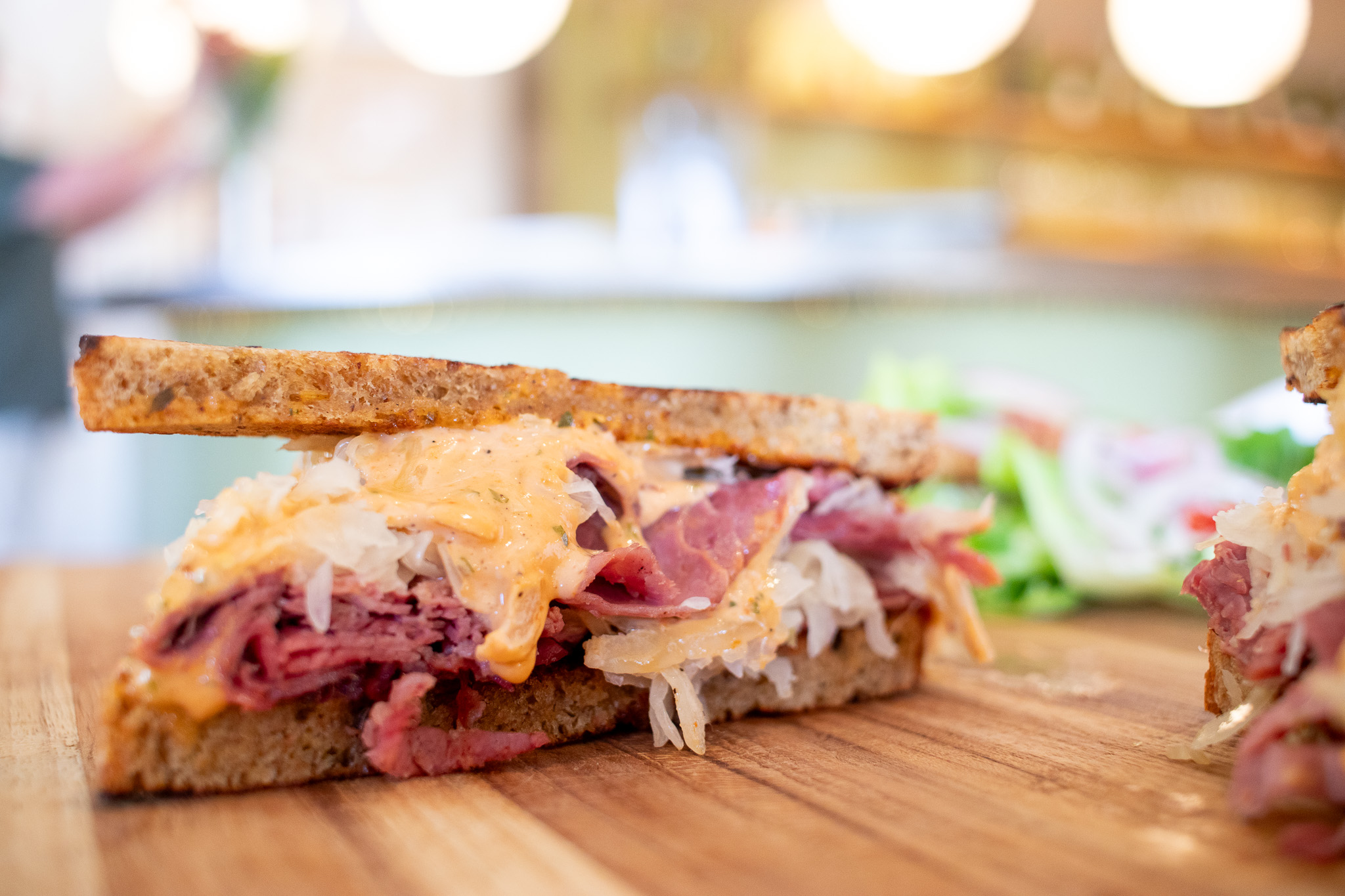 Toasted sandwich with pastrami, sauerkraut, and dressing on a wooden board.