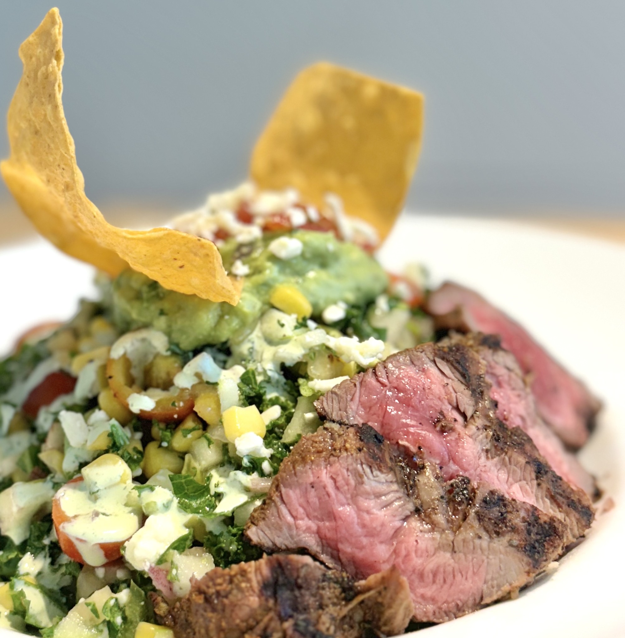 Sliced steak salad with guacamole, corn, and tortilla chips.