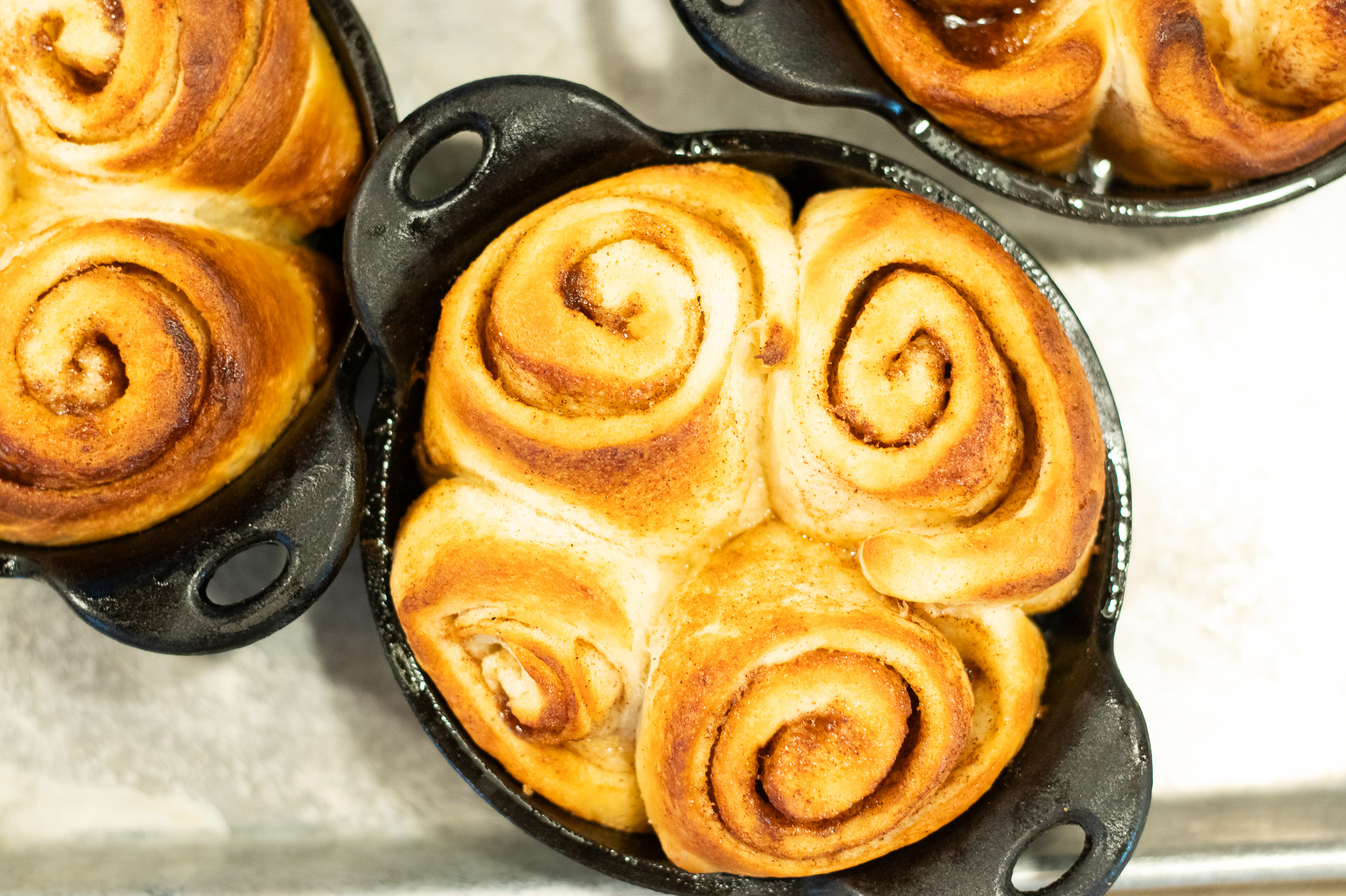 Three golden-brown cinnamon rolls in black cast iron serving dishes.