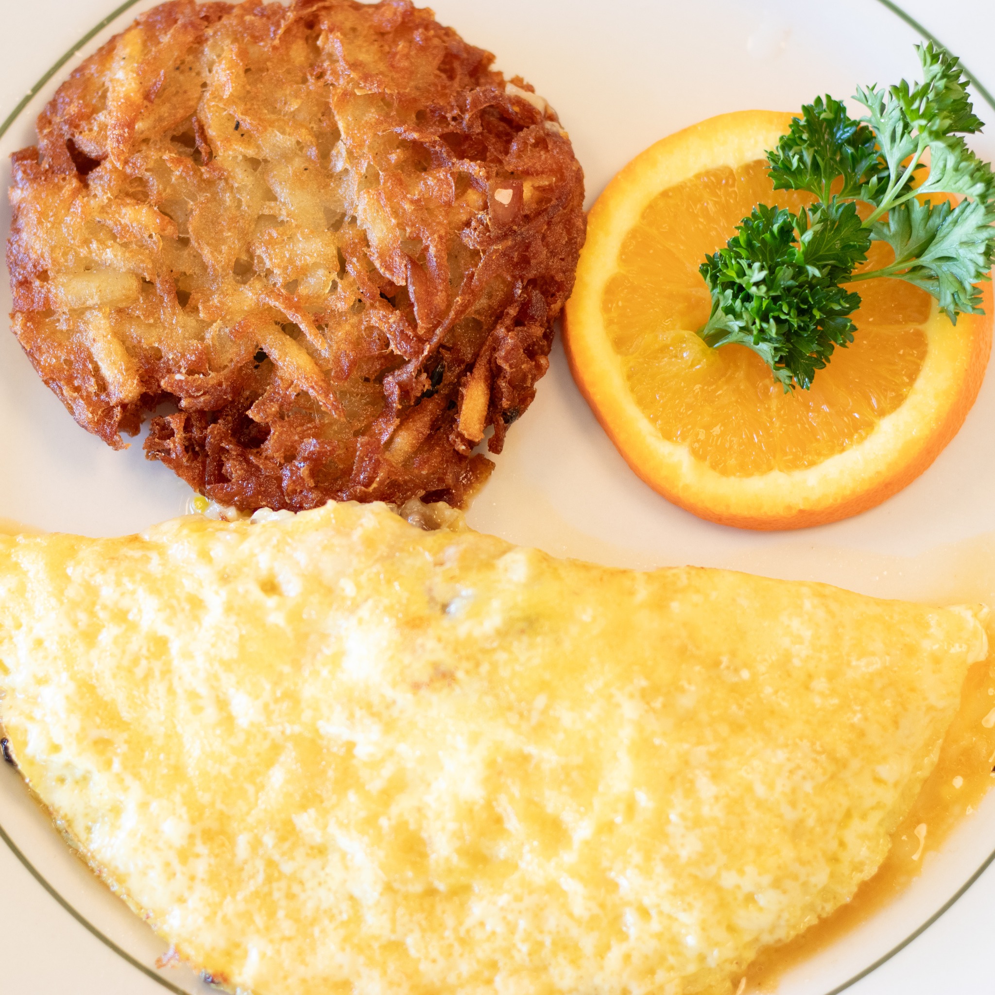 Golden hash brown, omelet, and orange slice with parsley on a white plate.