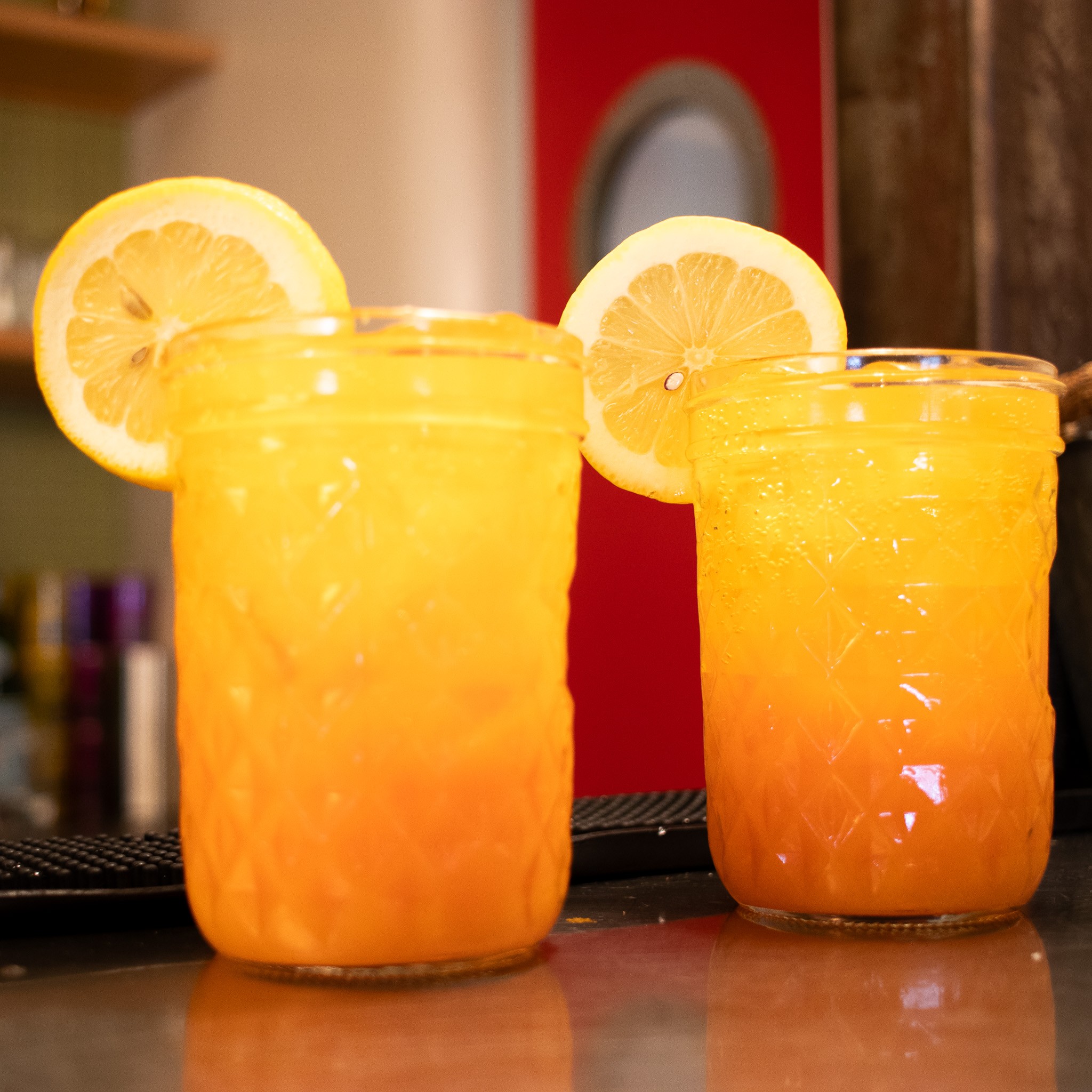 Two orange drinks with lemon slices on a bar counter.