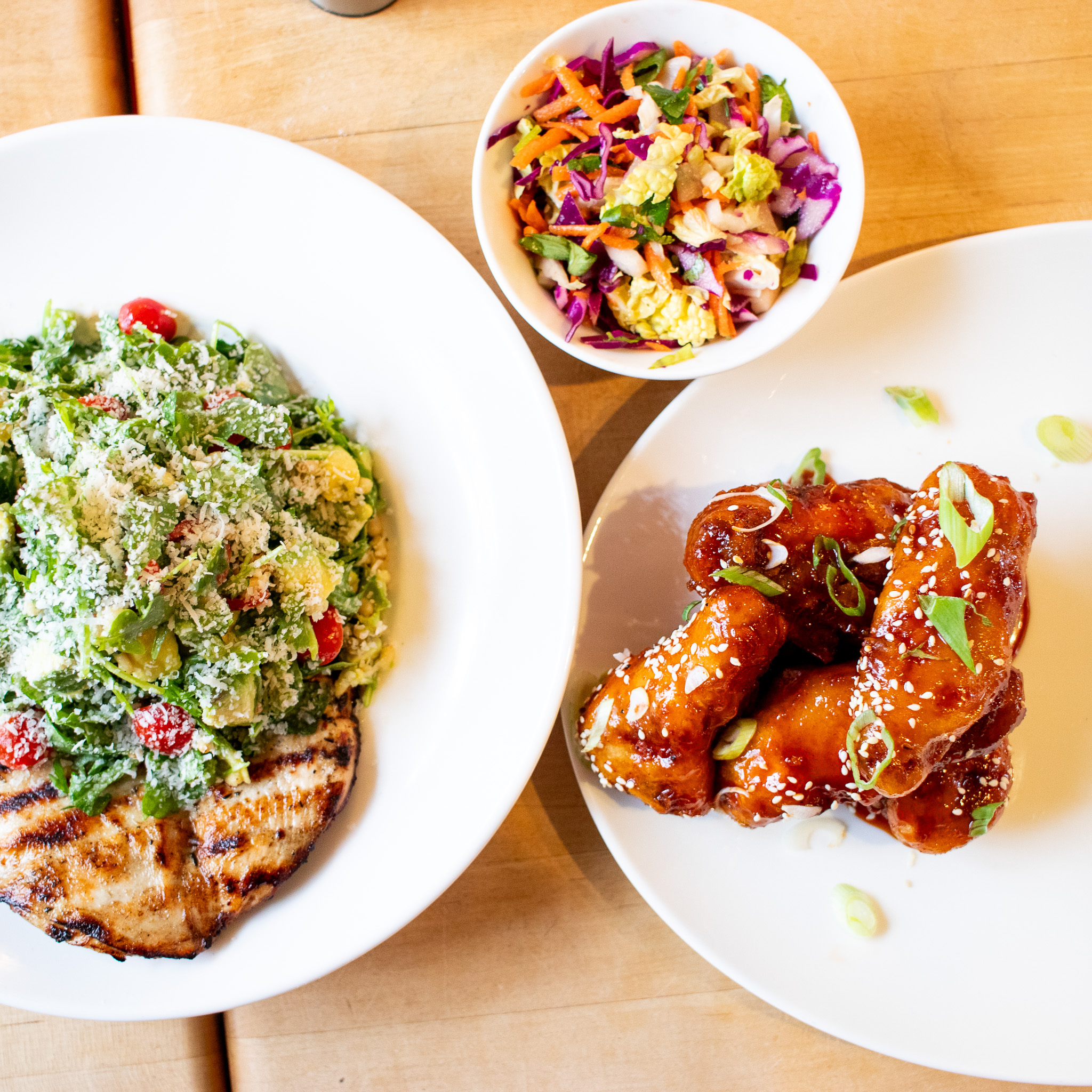 Top-down view of grilled chicken, salad, glazed wings, and coleslaw.