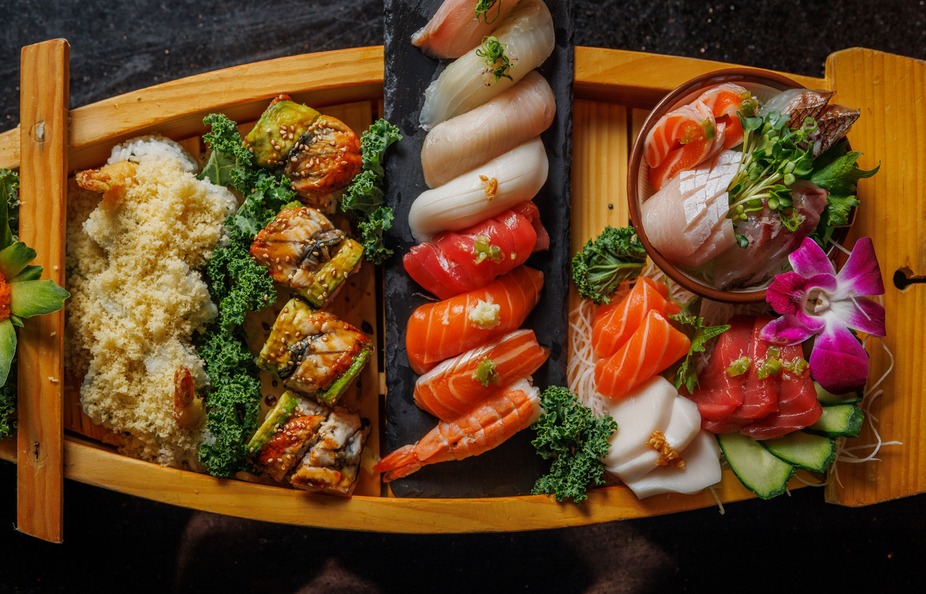 Assortment of sushi, sashimi, and rolls served in a wooden boat.