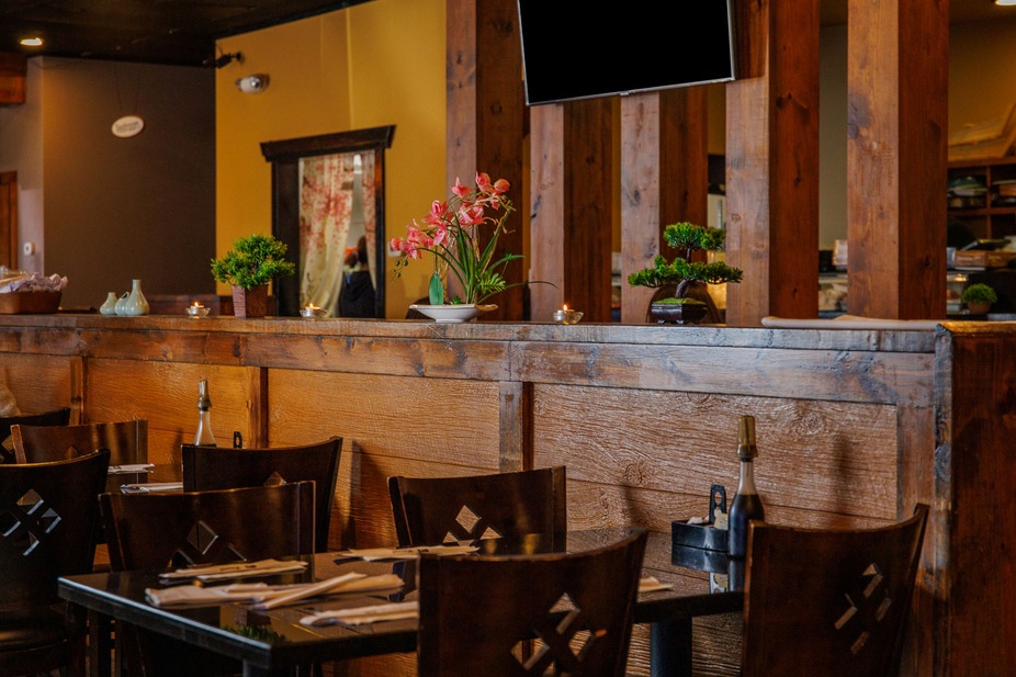 Interior of a restaurant with wooden paneling, tables, chairs, and decorative plants.