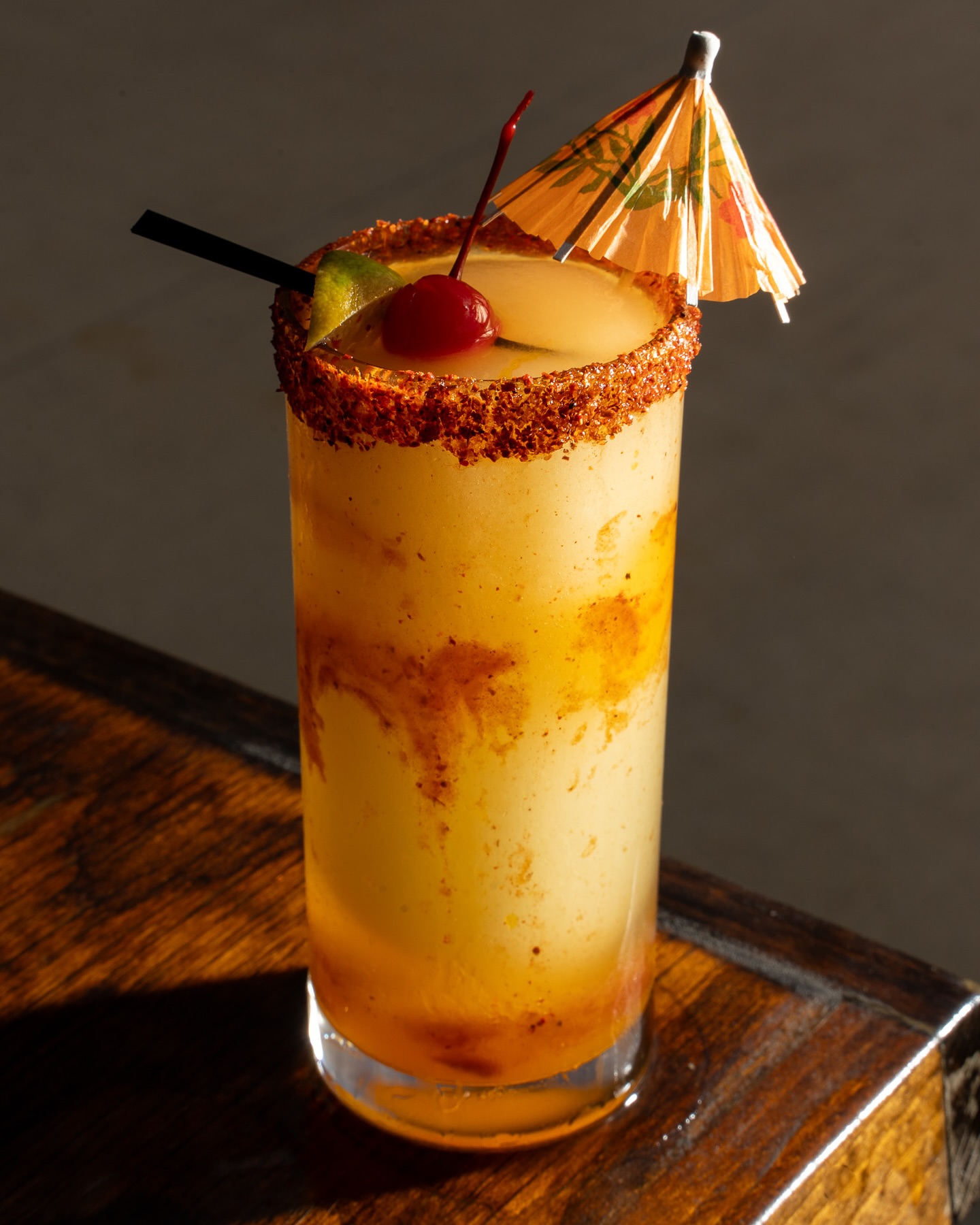 Tall yellow cocktail, spiced rim, cherry, lime, umbrella, and straw.