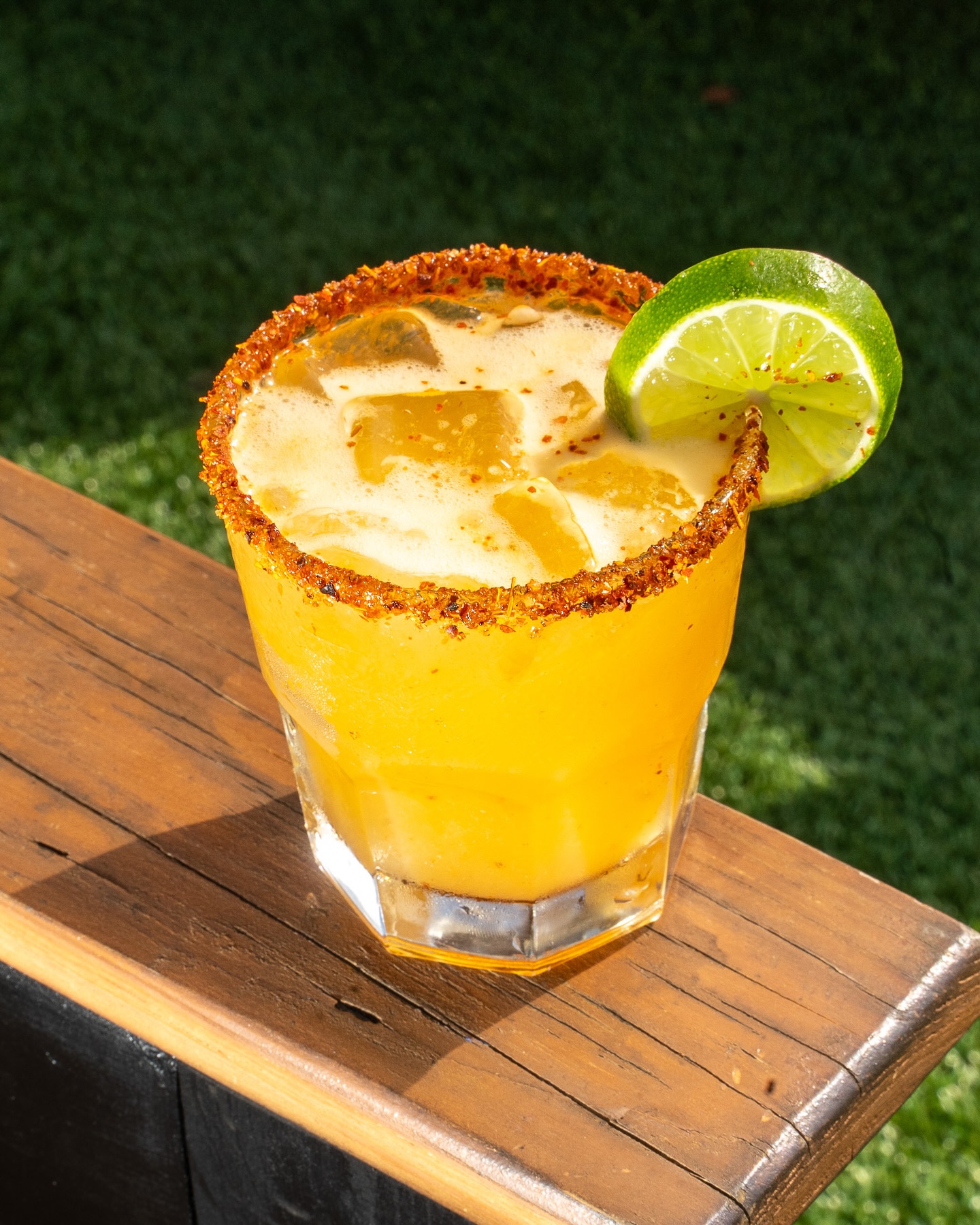 Yellow drink with chili-spiced rim and lime, on a wooden surface.