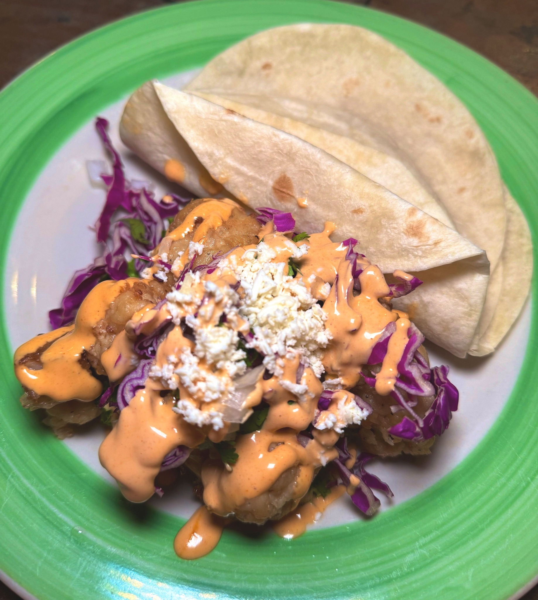 Cooked shrimp, orange sauce, cheese, cabbage, and tortillas on a plate.